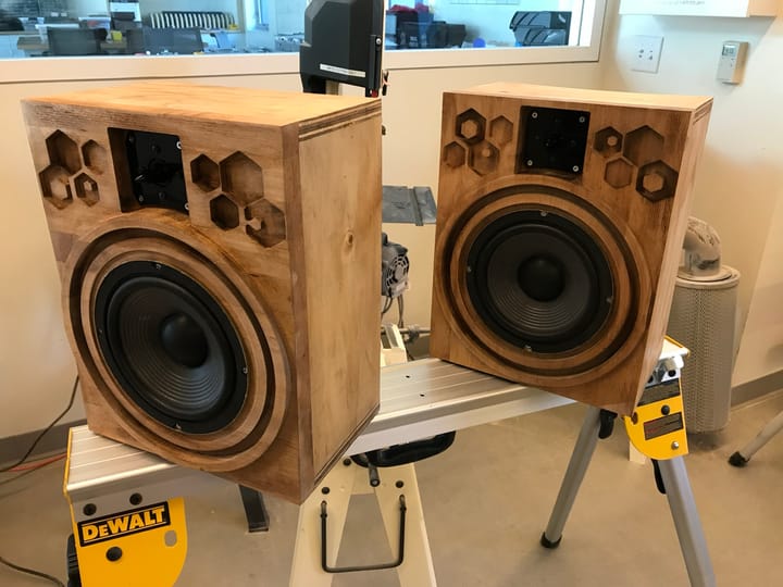 A pair of handmade wooden speakers with exposed drivers